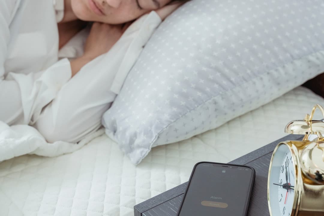 Une personne qui dort dans son lit, avec un réveil et un téléphone sur la table de chevet